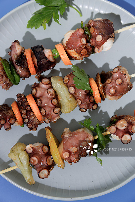 蓝色背景盘子里的章鱼蔬菜沙爹图片素材