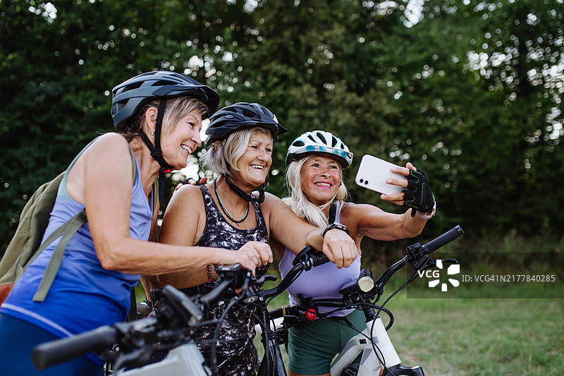 在自然中骑自行车旅行的三位老年朋友正在自拍。老年妇女在低强度路线上骑电动自行车。图片素材