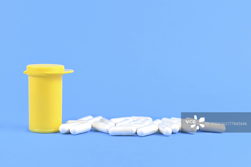 亮蓝色背景上黄色药瓶旁的胶囊药丸图片素材