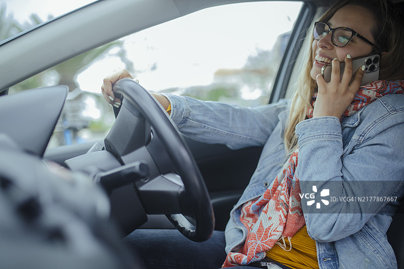 微笑的女人一边开车一边用手机交谈。图片素材