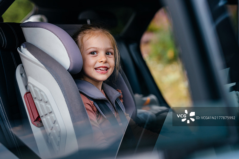 微笑的孩子安全地坐在汽车座椅上，享受家庭旅行图片素材