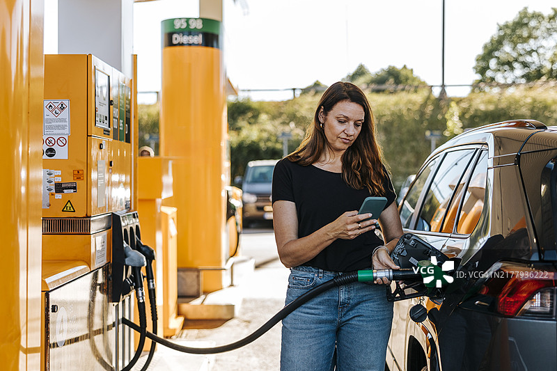 在加油站给汽车加油时使用智能手机的女人图片素材