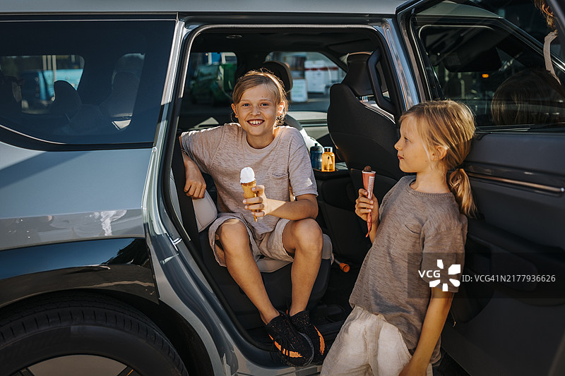 微笑的男孩坐在车里拿着冰淇淋，哥哥靠在门上图片素材