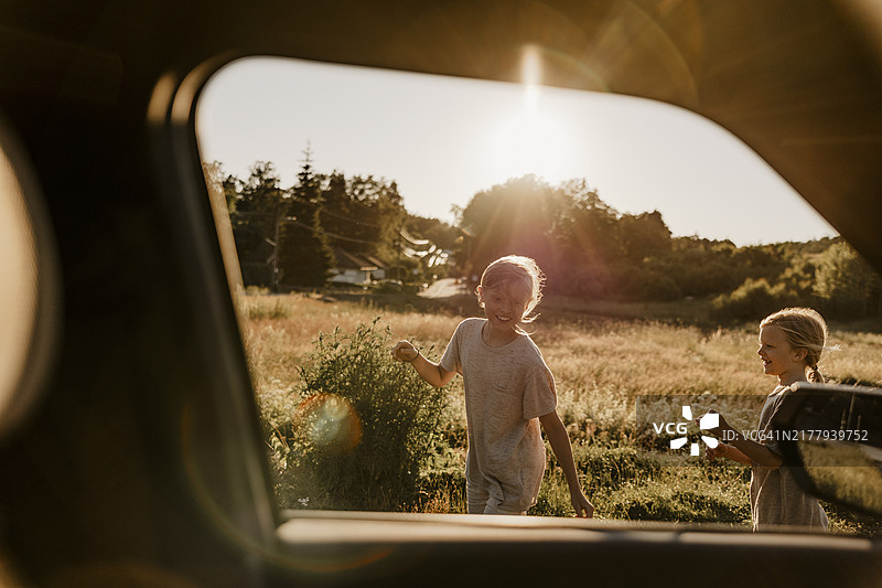 快乐的兄弟姐妹在草地上玩耍（透过车窗）图片素材