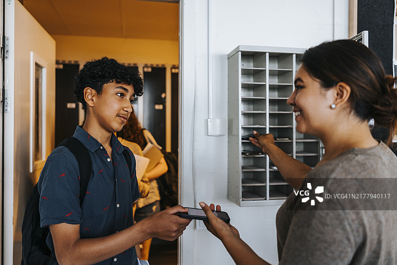 微笑的女老师从站在教室门口的少年那里收智能手机图片素材