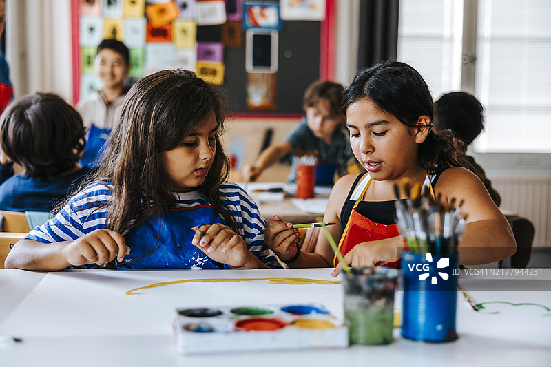 在小学美术课上，女学生们一边绘画一边讨论图片素材