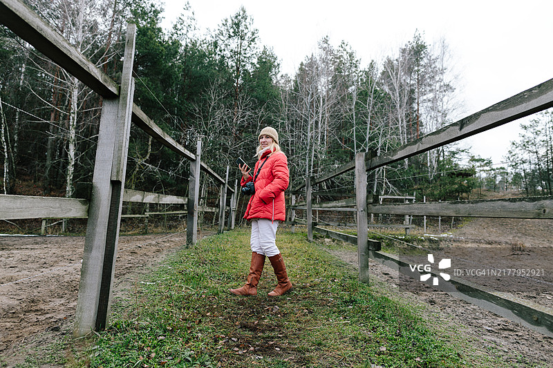 穿着红色夹克在多云的乡村围栏区域行走的女人图片素材