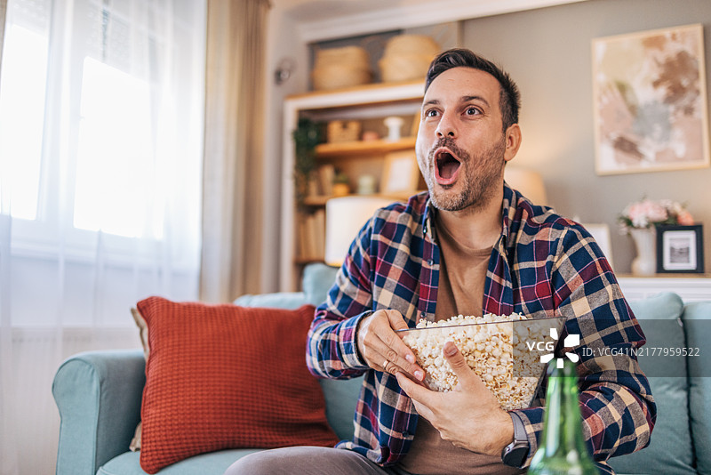 坐在客厅沙发上看比赛吃爆米花喝啤酒的中年男子图片素材
