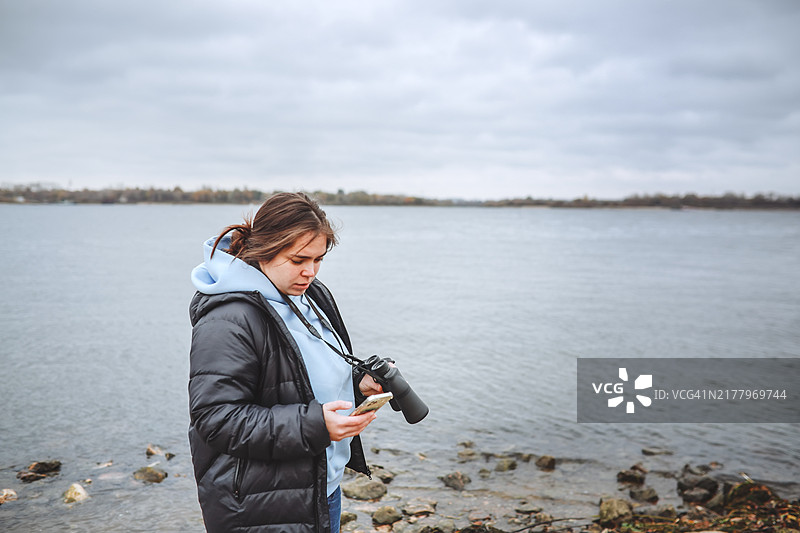 清晨观鸟，穿连帽衫和夹克的女人拿着双筒望远镜和智能手机图片素材