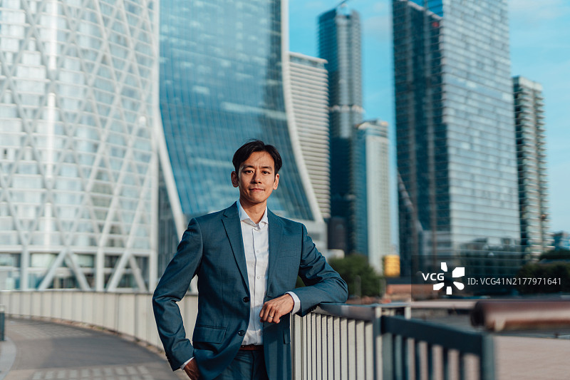 自信的亚洲商人站在现代大都市金融区的办公楼前图片素材