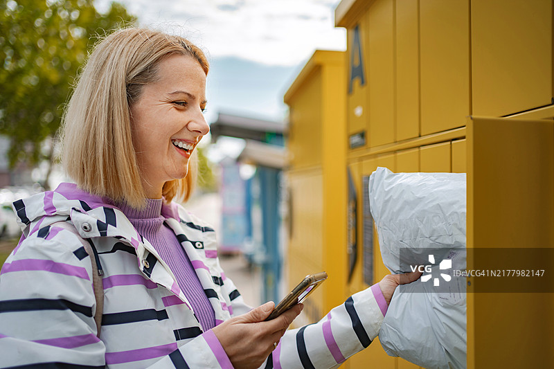 女性使用智能手机从自动取件柜取包裹图片素材