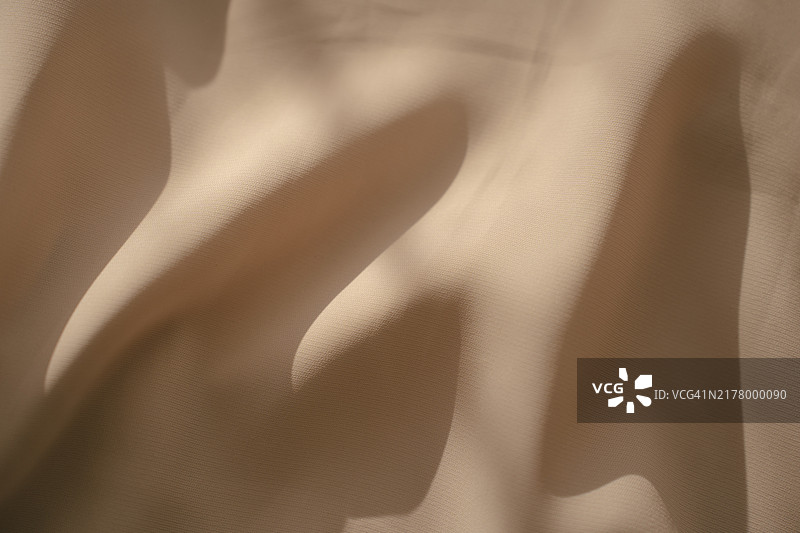 米色织物抽象背景，奶油色纺织品在柔和阳光下褶皱图片素材