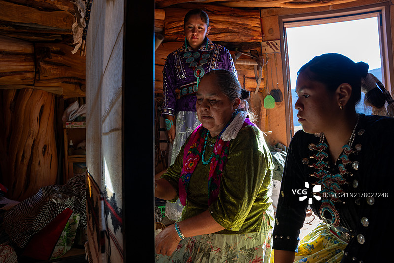 一位纳瓦霍族奶奶在霍根向两个孙女展示如何编织传统的纳瓦霍族服装图片素材