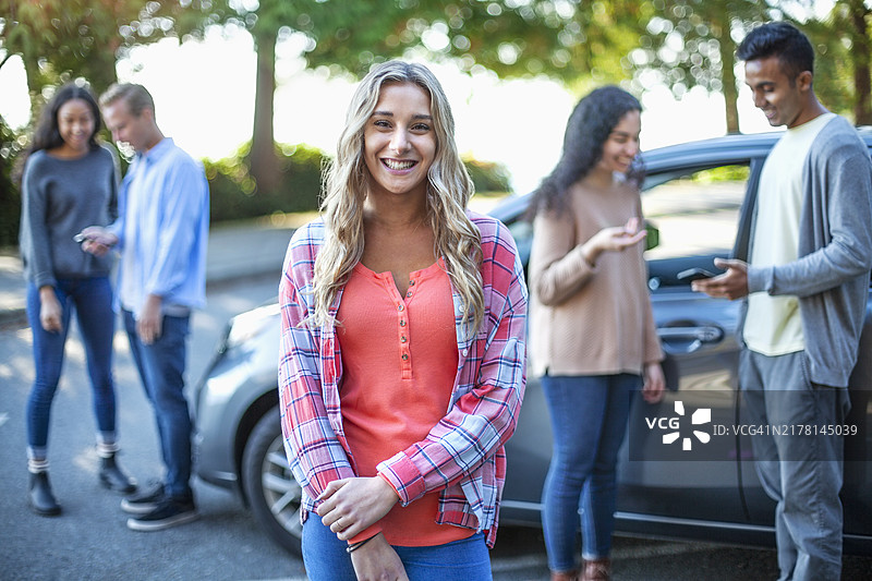 年轻的白人少女站在汽车前，一群多种族朋友在停车场外的肖像图片素材