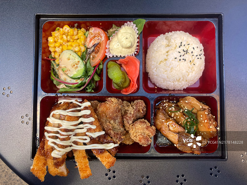 照烧、日式炸鸡和吉列鸡肉便当盒，配米饭、沙拉、酸黄瓜和腌姜图片素材