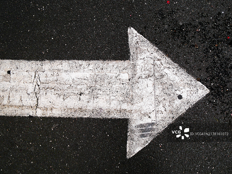 伦敦，英国街道上灰色沥青上的一支涂漆和氧化的白色箭头。粗糙的纹理。阳光。自然色彩。图片素材