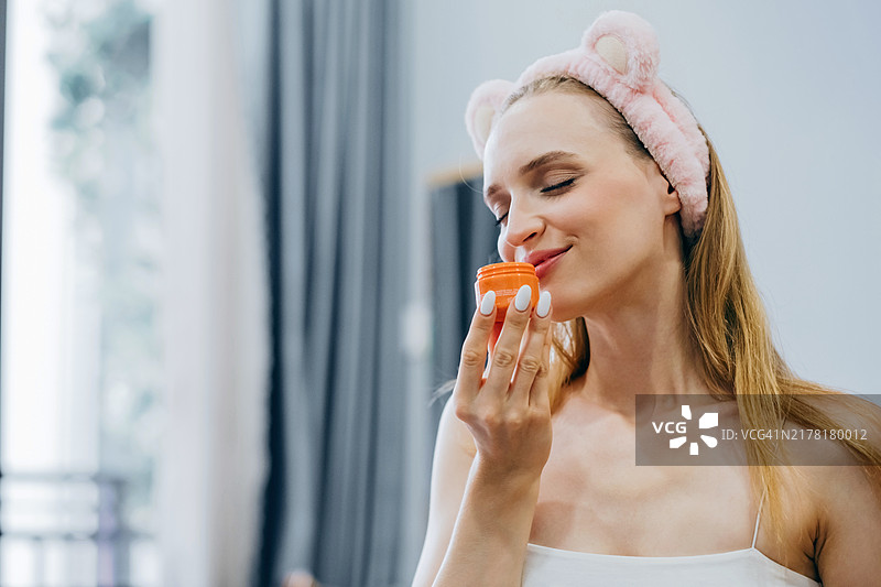 年轻女子面带微笑，享受护肤品的香味，展现美容过程中的幸福和自我护理图片素材