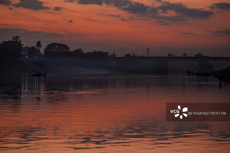孟加拉国西尔赫特的苏尔马河上空的火红日落与远处的船只图片素材