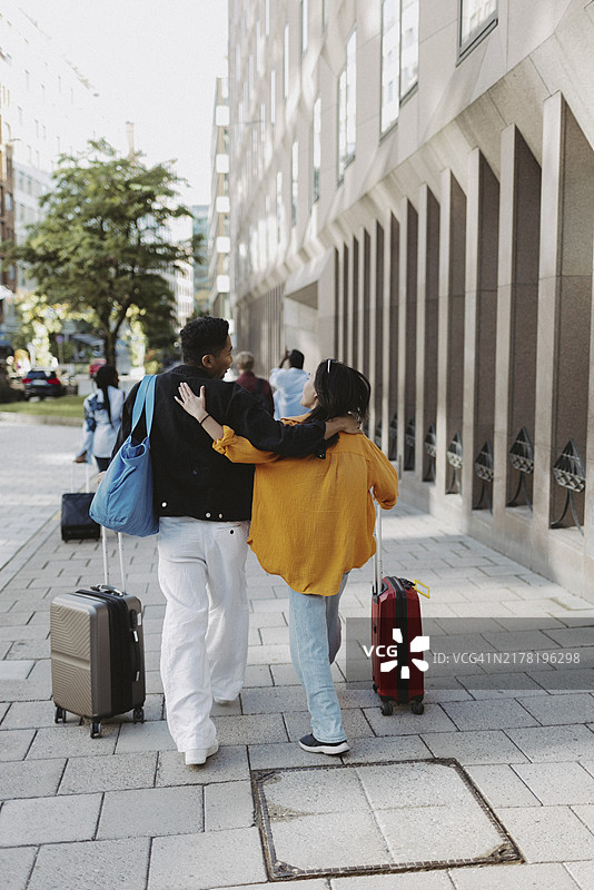 男性和女性朋友手推行李箱在人行道上行走（后视图）图片素材