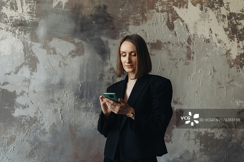 在灰色纹理墙边使用智能手机的年轻女商人图片素材