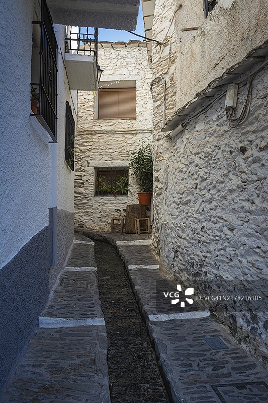 阳光明媚的天空下，西班牙格拉纳达阿尔普哈拉斯的狭窄石墙小巷，椅子上放着一盆植物图片素材