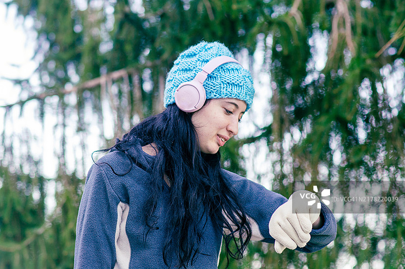 在大自然中跑步，她听着音乐并查看手表以掌握时间。图片素材