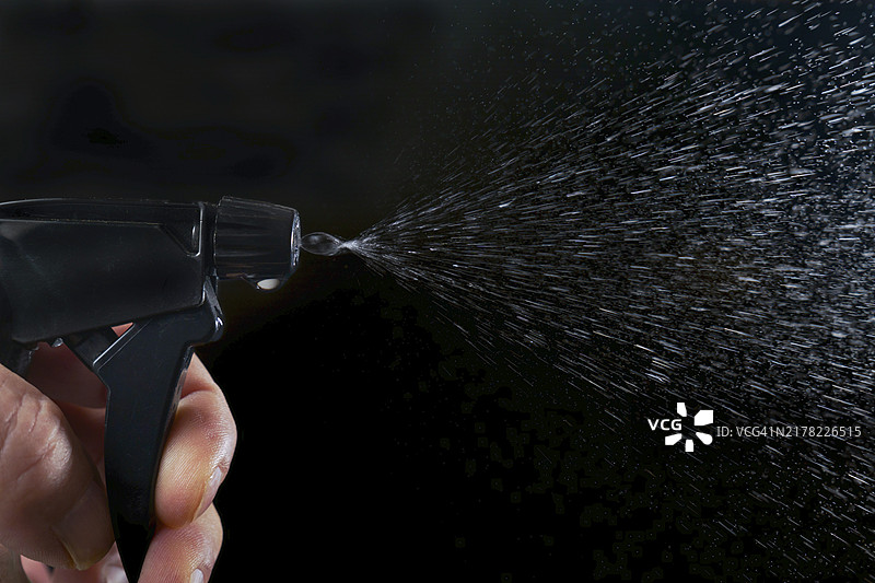 男人按下喷雾器的扳机，在黑色背景上喷洒水滴图片素材