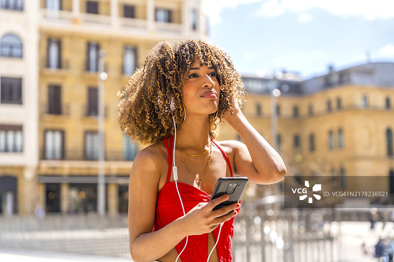 在城市中使用手机听音乐的西班牙裔女子图片素材