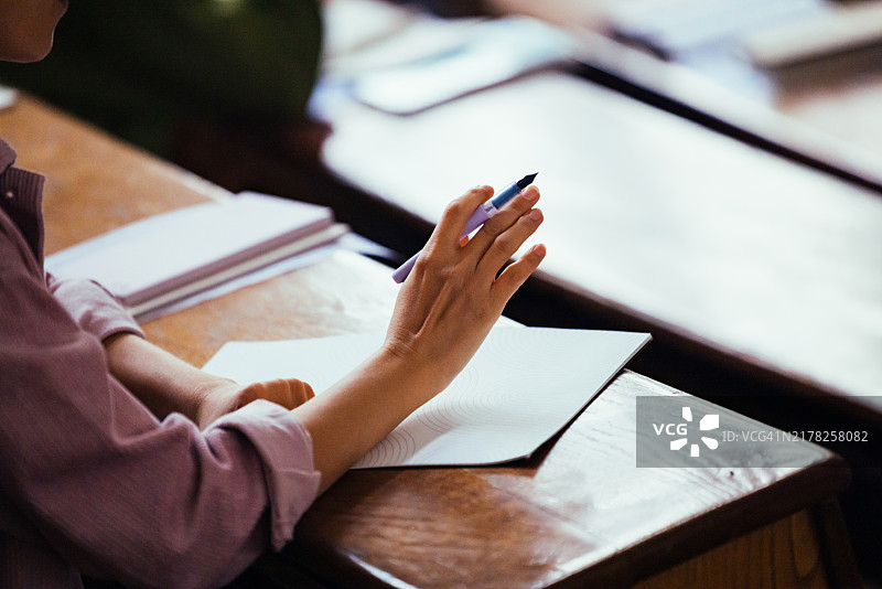 教室里的人在笔记本上用笔书写的特写图片素材