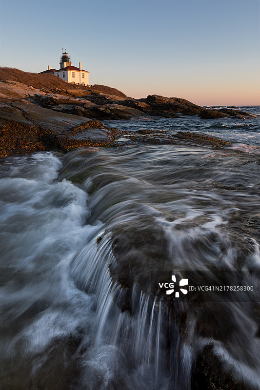 日落时分的灯塔，水流冲刷着岩石图片素材