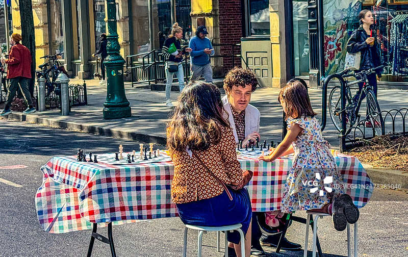 一家人在纽约市上西区开放街道的桌旁下棋图片素材
