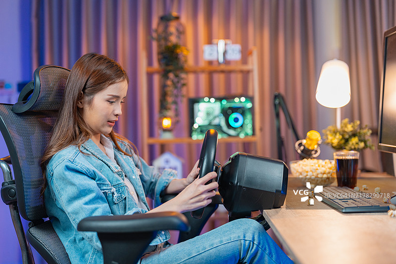 年轻的亚洲女孩坐在驾驶模拟器上，佩戴耳机，注视着4D屏幕，在家中的游戏室里享受着夜晚霓虹灯下的游戏乐趣。图片素材