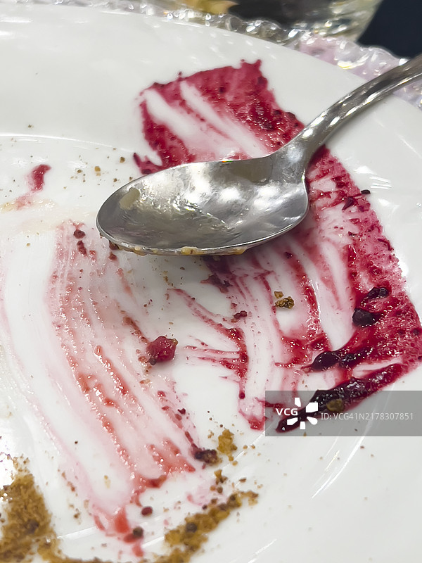草莓甜点残余物和勺子的盘子，展示酱汁和面包屑的痕迹图片素材