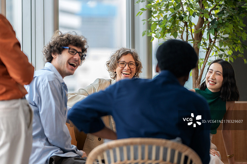 一群多元化的员工在现代化的办公环境中休息，愉快地聊天和交谈。气氛反映了一个支持和协作的工作场所，团队成员分享想法并建立友谊图片素材