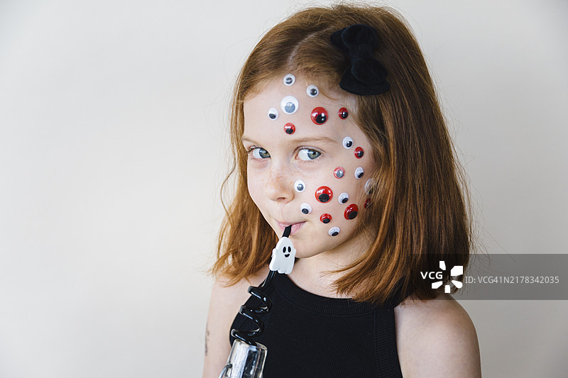 脸上贴着眼睛贴纸的女孩用吸管喝东西图片素材