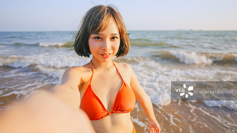 在海滩上自拍的穿红色比基尼的年轻女子肖像图片素材