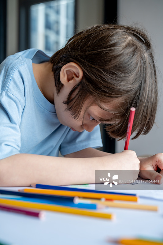 男孩用彩色铅笔在桌子上专心绘画图片素材
