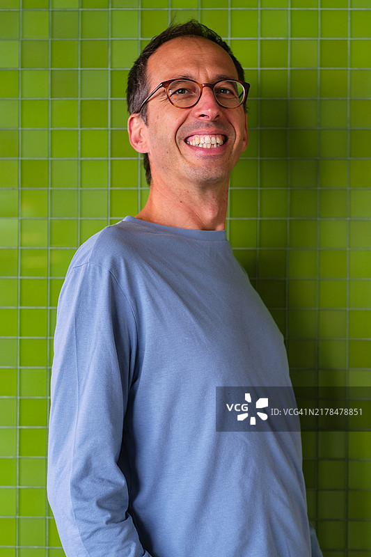 自信的男人穿着浅蓝色T恤，站在绿色瓷砖墙前。图片素材
