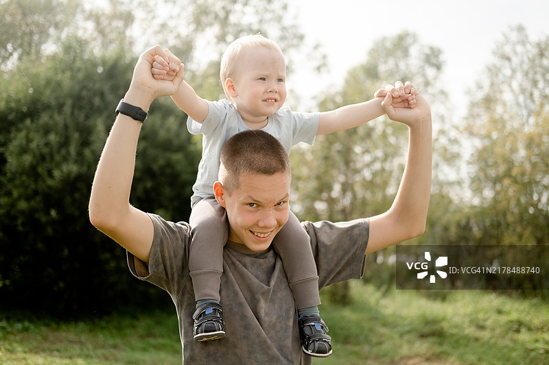 孩子们在户外玩耍：小男孩坐在哥哥的肩膀上，一家人在夏日公园里散步图片素材