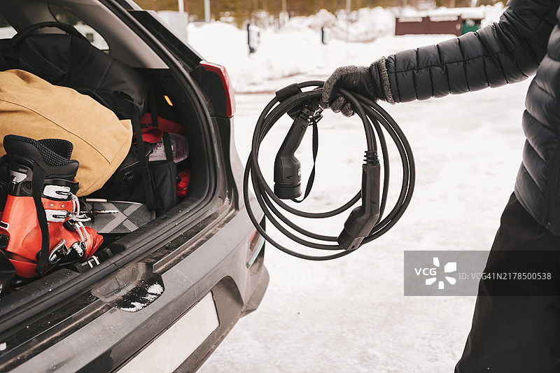 一名男子将充电线插入电动汽车后备箱的特写镜头。图片素材