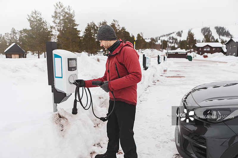 一名男子在冬季运动度假村的充电站为电动车充电。图片素材