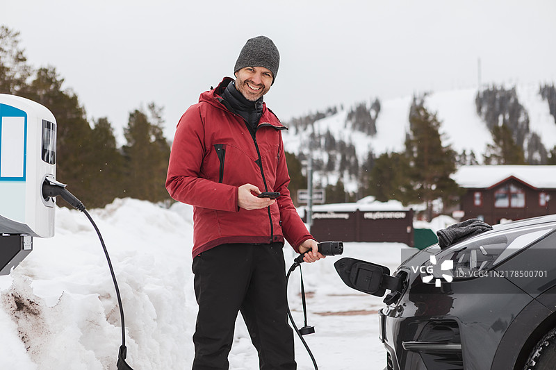 一名男子在冬季运动度假村的充电站为电动车充电。图片素材