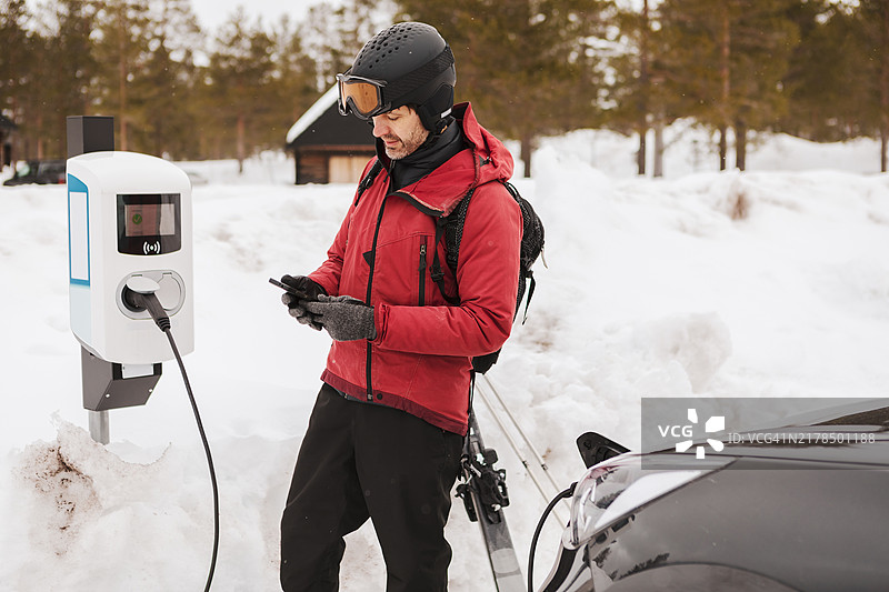 一名男子在冬季运动度假村的充电站为电动车充电。图片素材