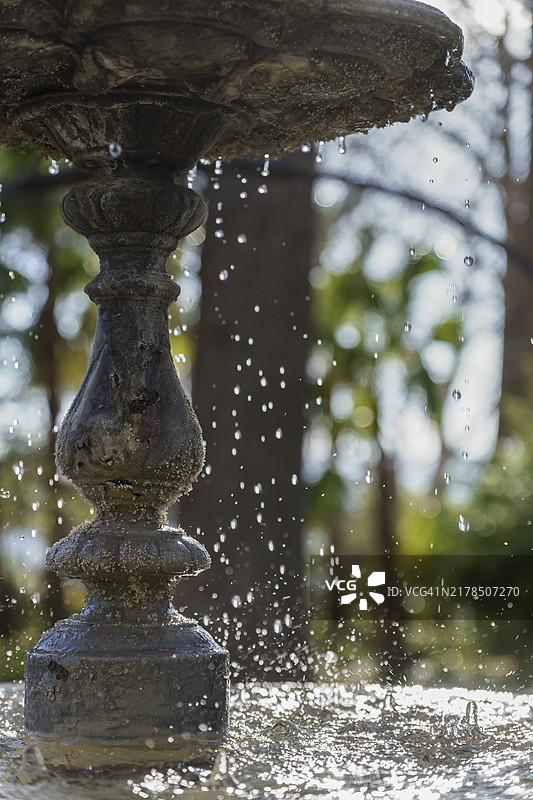 带有飞溅水的公共喷泉侧面，背景是蓝天和公园树木图片素材