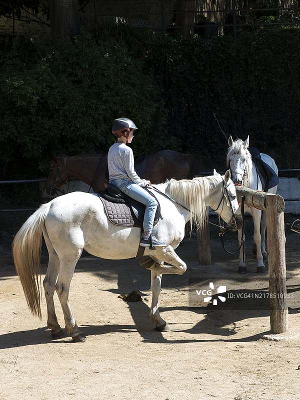 侧面视图的小男孩骑着一匹小白马图片素材