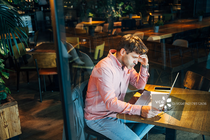 在舒适的咖啡馆环境中远程使用笔记本电脑工作，同时查看电子邮件并感到焦虑的商人图片素材
