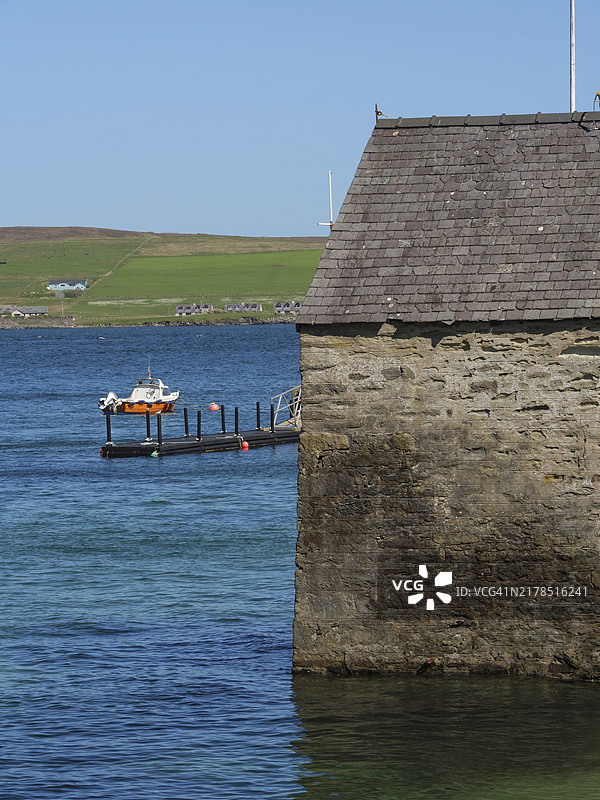 海滨石板屋顶的石头建筑，背景是带有小船的码头，英国苏格兰设得兰群岛勒威克图片素材