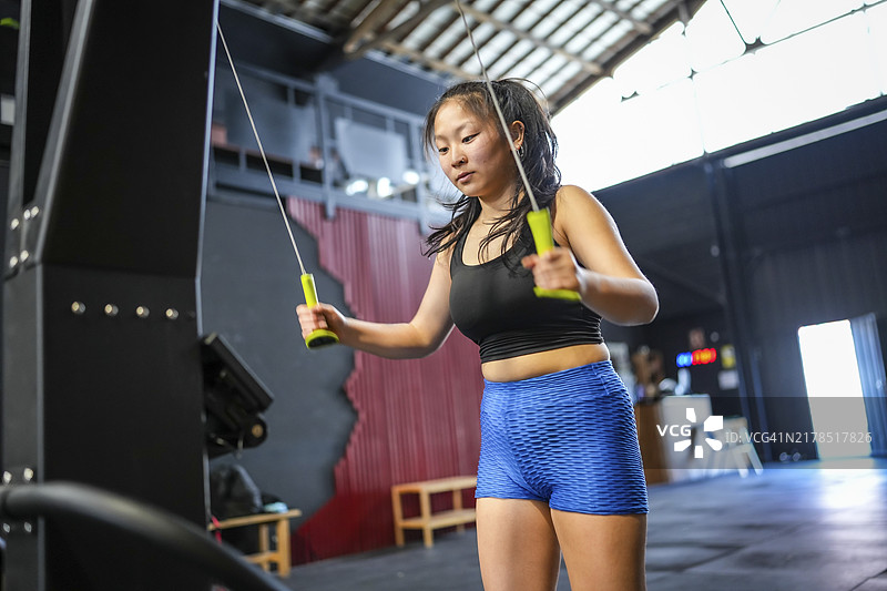 健身房里健壮的中国年轻女人使用高位下拉器械的仰视角度照片图片素材