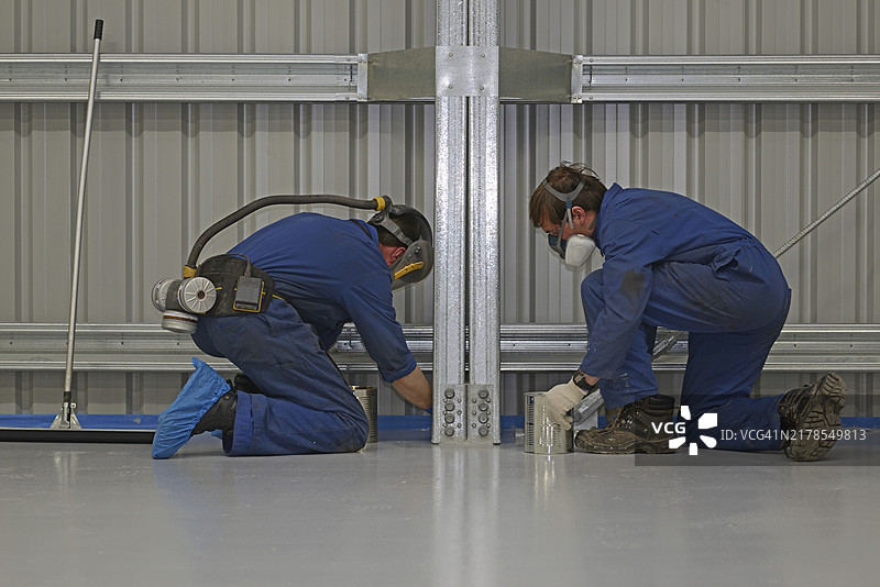 两名商人在墙边使用环氧地坪材料切割，其余团队成员使用滚筒完成工作图片素材