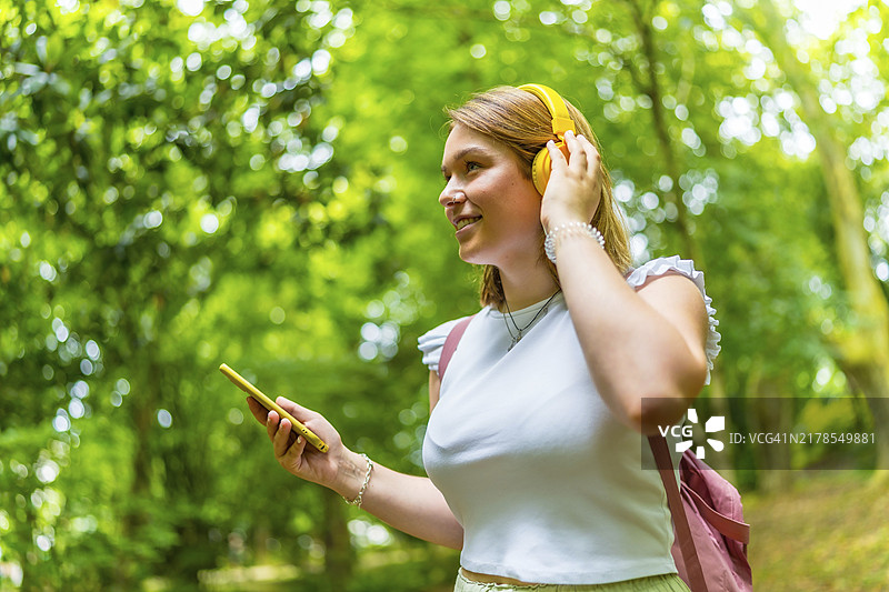 快乐的白人年轻妇女在森林里徒步旅行时，用手机听音乐图片素材